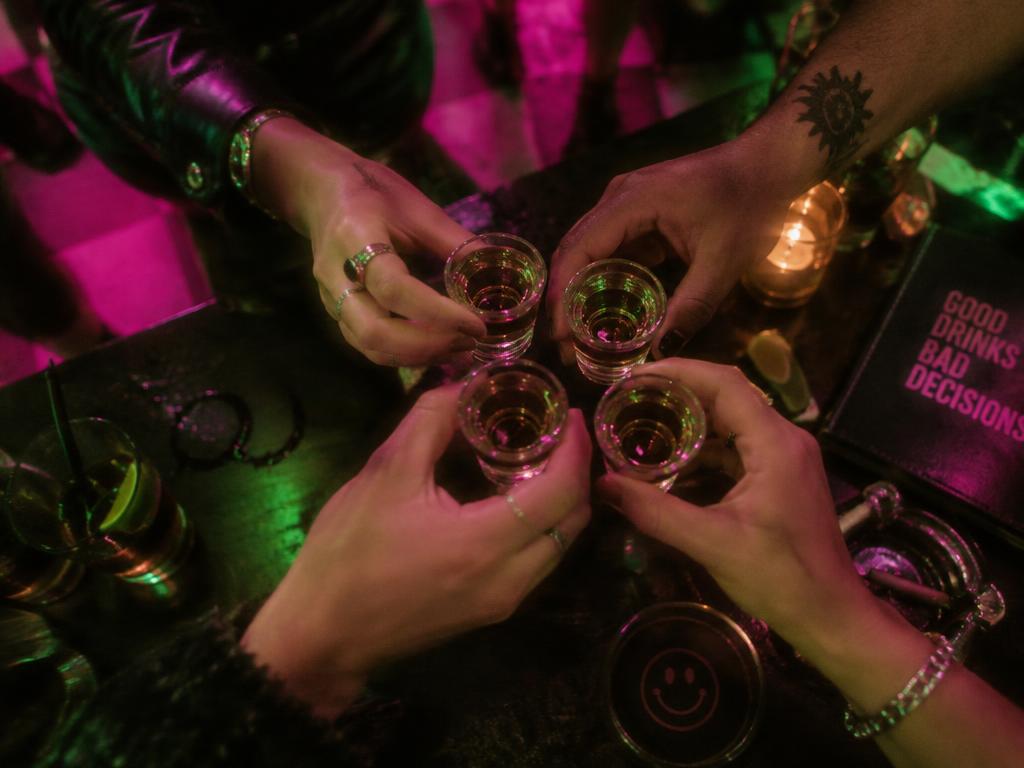Friends raising shot glasses together in a dark neon-lit bar